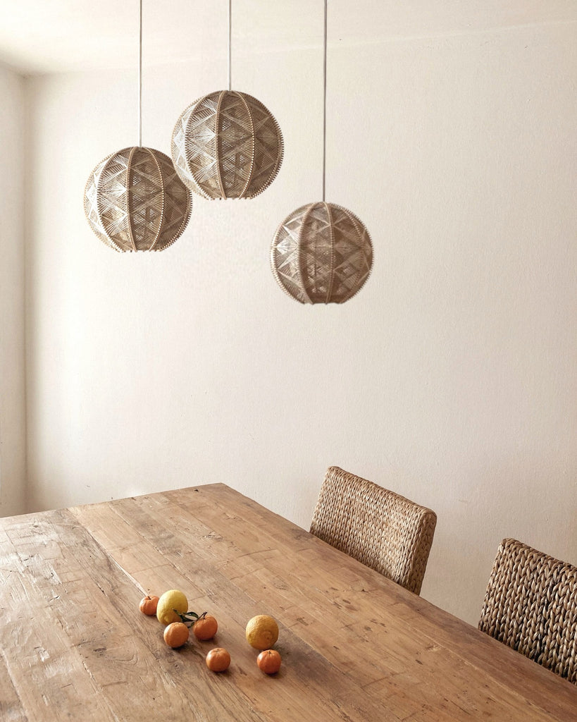 drei runde Hängeleuchten aus Birkenholz umwebt mit beigem Leinengarn hängen versetzt über einem Holztisch mit Zitrusfrüchten
