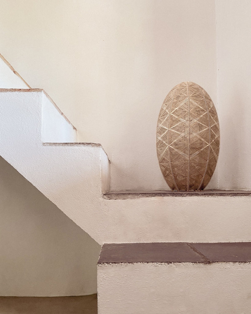 eine handgewebte Lampe aus Birkenholz und Leinengarn in Naturtönen auf einer mediterranen Treppe